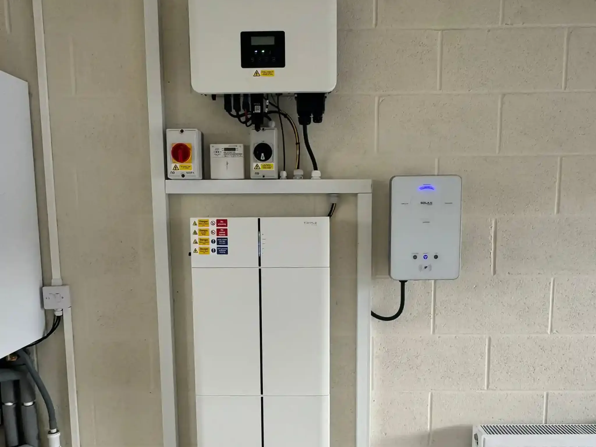 A hybrid inverter, a stacked home battery and an EV charge point installed together on a domestic garage wall