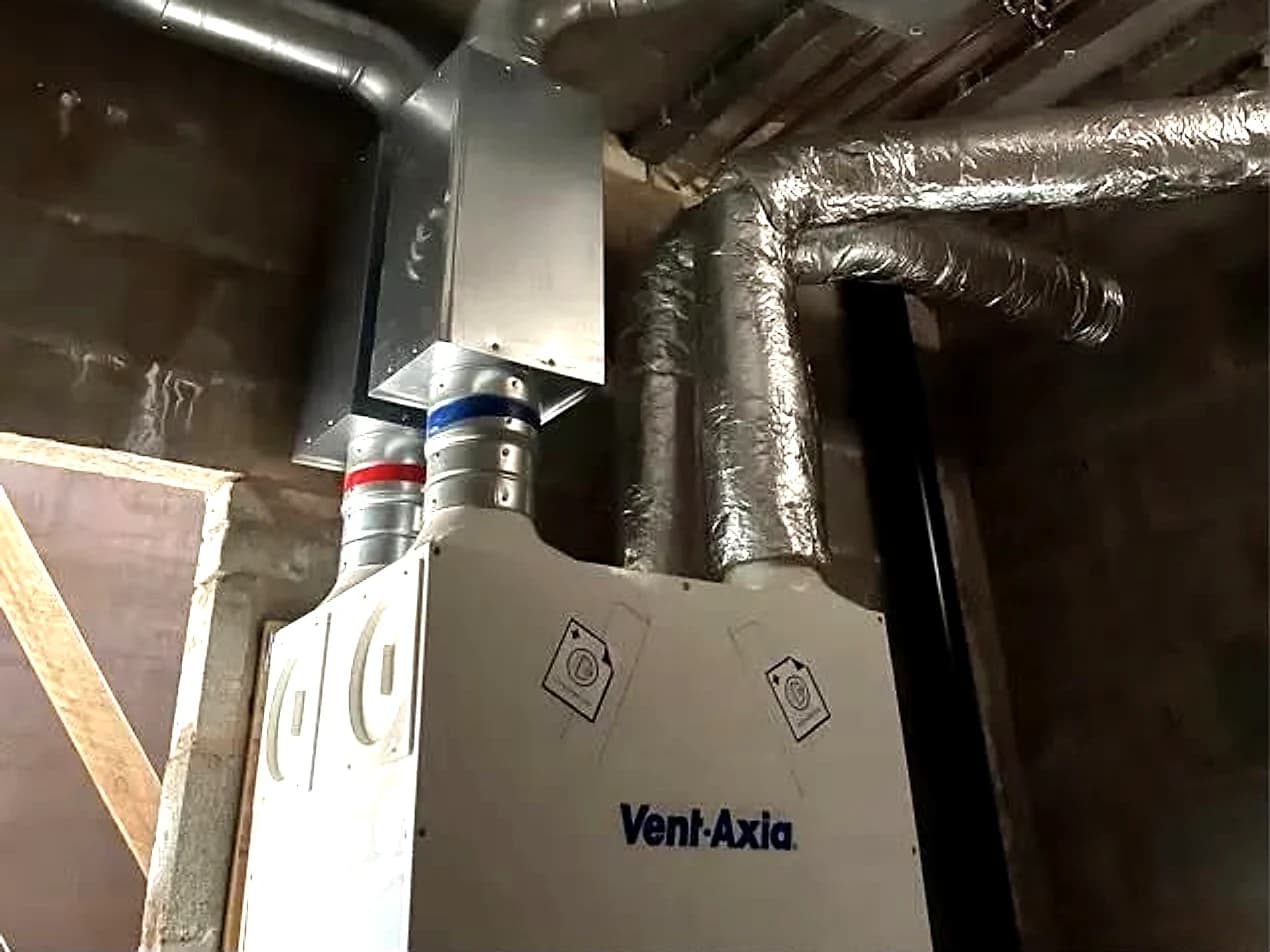 An MVHR heat recovery unit with rigid ducting and red and blue radial ducts running into a plenum above it