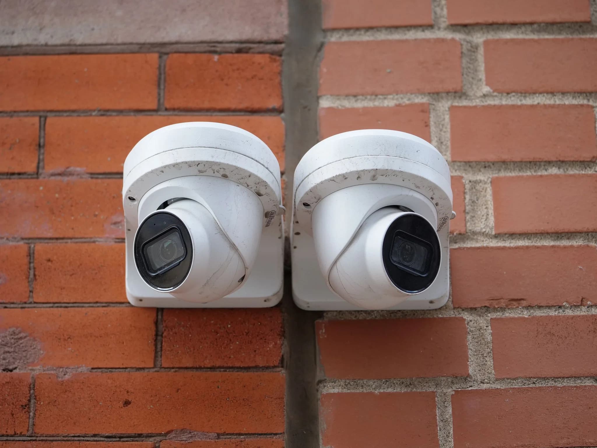 Two dome CCTV cameras mounted side by side on a red brick wall