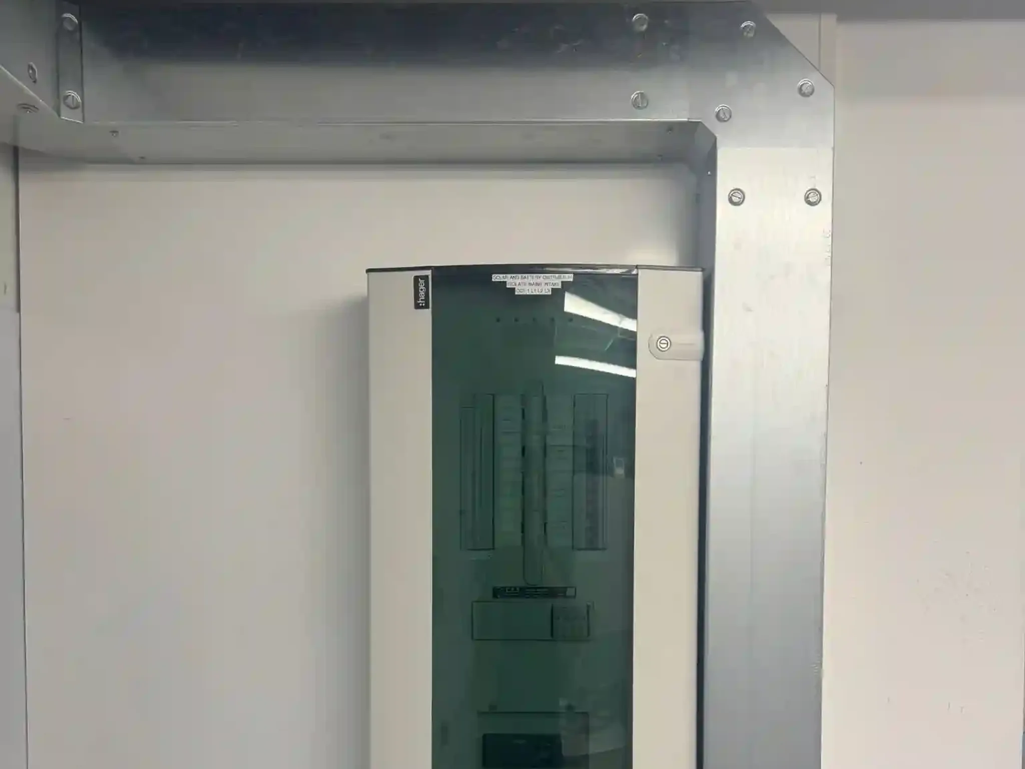 A three phase distribution board on a wall with galvanised trunking running beside it and across a steel beam above